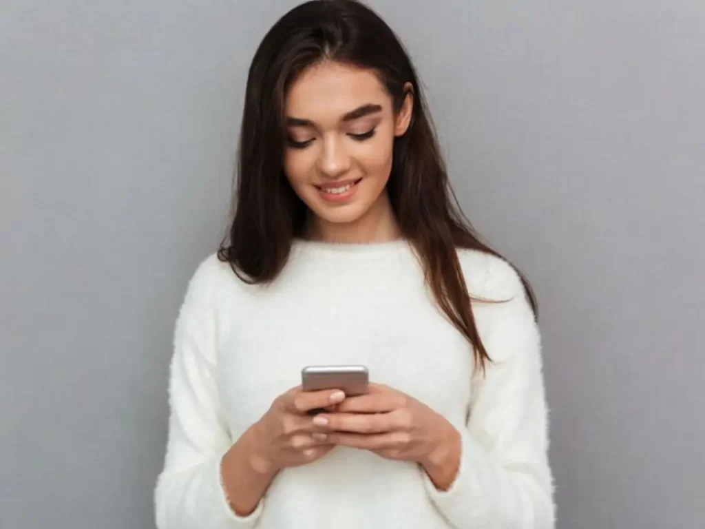 mulher mexendo no celular na parede cinza