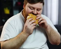 Homem de camisa branca comendo hamburguer de carne