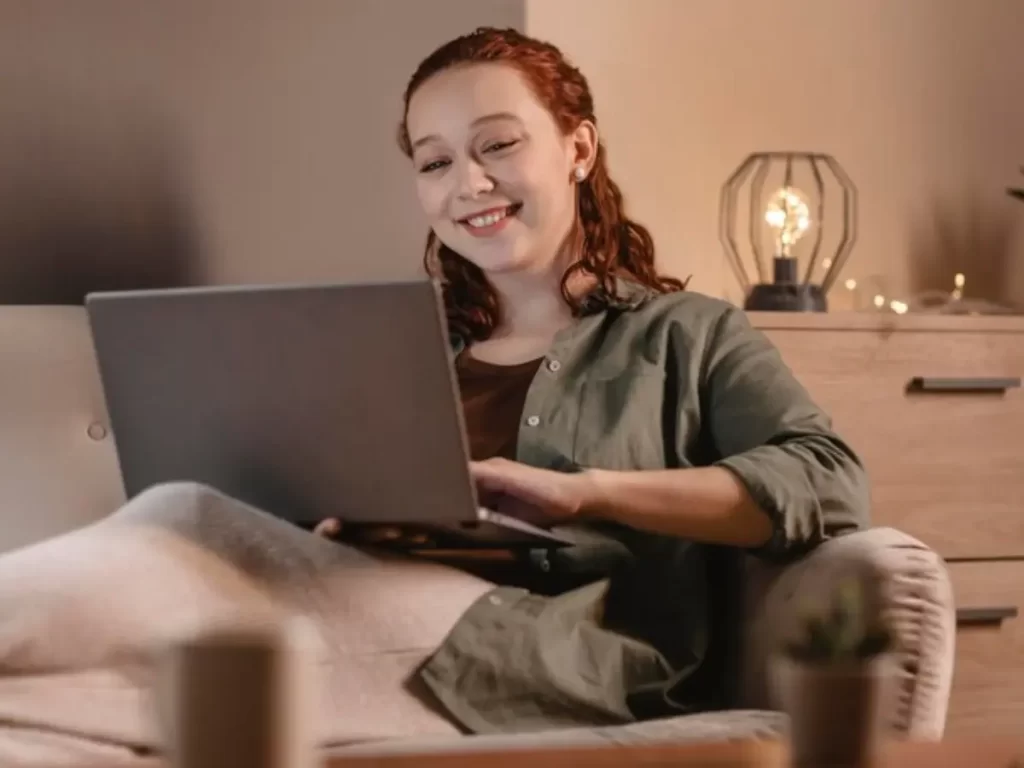 mulher sorrindente usando laptop em casa no sofá